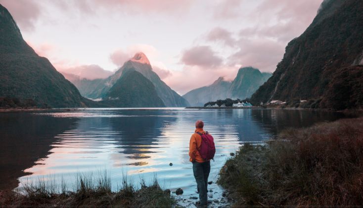 A man standing by the shore in Milford Sound, New Zealand.