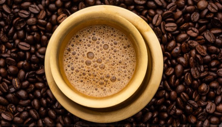 A cup of black coffee surrounded by coffee beans.