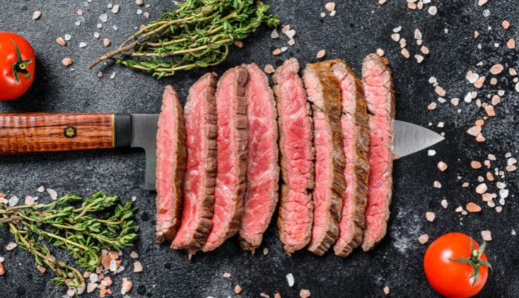 A medium rare steak cut into strips, laid out on a cutting board.