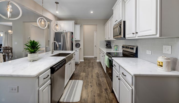 A kitchen with white cupboards and brown wooden flooring.