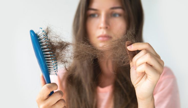 A woman pulling clumps of hair out of a blue brush.