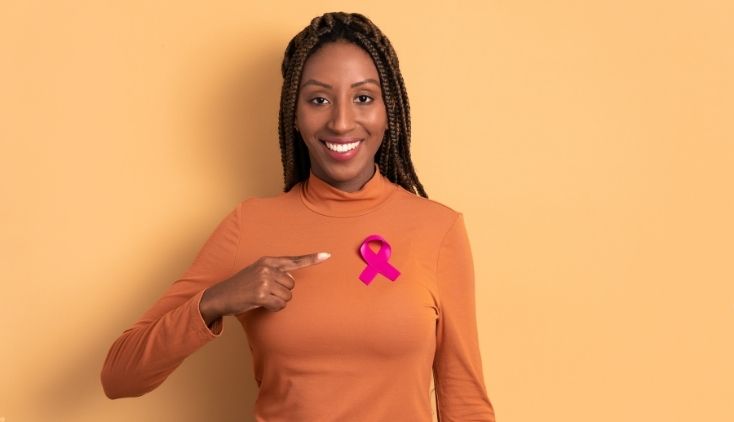 A woman in an orange shirt, wearing a pink breast cancer ribbon.